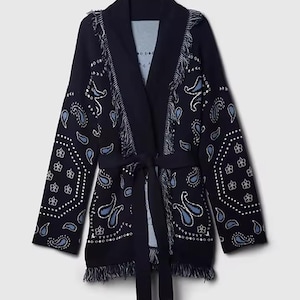 May include: A dark navy blue open-front cardigan featuring a white and light blue paisley pattern. The garment includes a matching tie belt at the waist, long sleeves, and decorative fringe detailing along the shawl collar and the bottom hemline.
