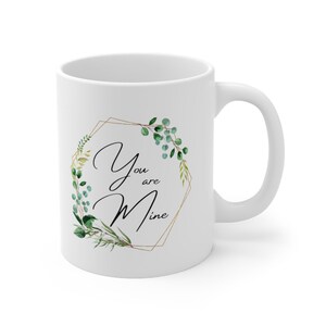 May include: White ceramic mug featuring a gold geometric frame and green foliage design. The text "You are Mine" is written in black script within the frame.