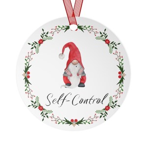 May include: A white round Christmas ornament with a red and white gnome wearing a red hat and holding a white bag. The gnome is surrounded by a green wreath with red berries and the text "Self-Control" is written below the gnome.