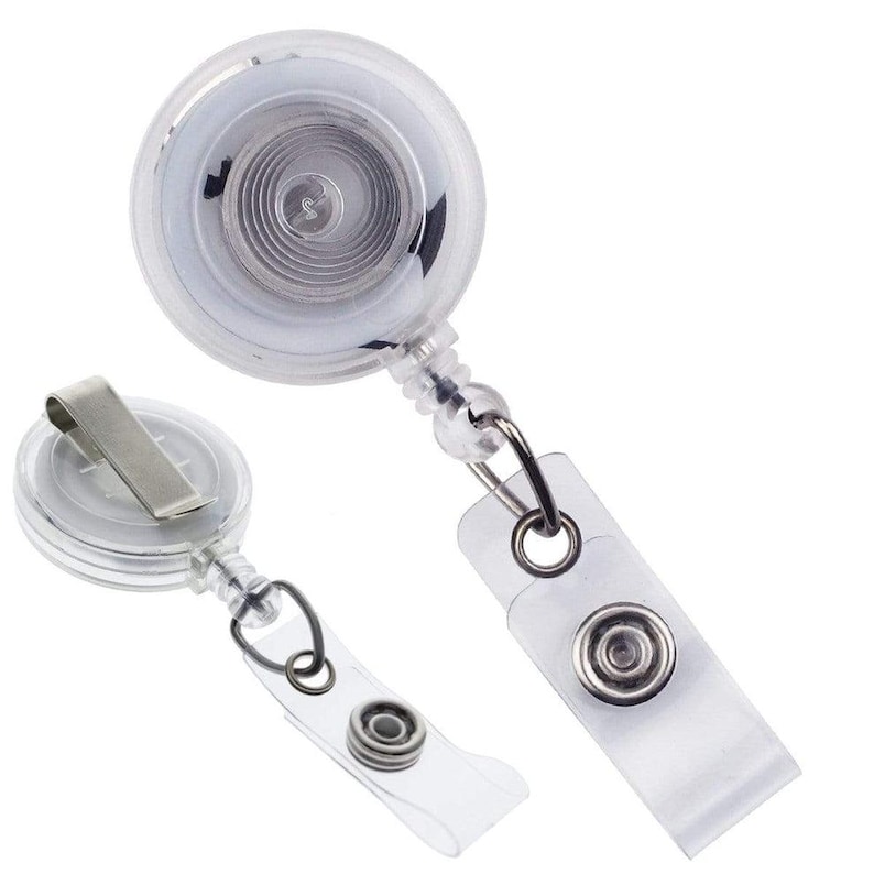 May include: Two clear plastic retractable badge holders with metal clips and snap closures. The badge reels have a circular design with a visible internal spring mechanism. One has a metal clip, and the other has a clear plastic strap.
