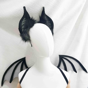 May include: Black bat ear headband with fluffy accents and matching black bat wings with clear membrane. The costume set is displayed on a white mannequin, perfect for Halloween or cosplay.