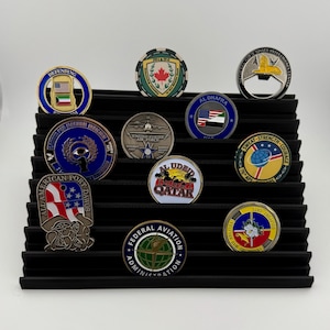 May include: A black display rack with 10 round, colourful challenge coins. The coins feature various designs, including flags, military emblems, and logos. The coins are arranged in rows on the rack.