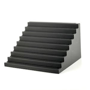 Puede incluir: Un expositor negro escalonado con diseño de escalera. El expositor tiene múltiples plataformas horizontales, creando un efecto escalonado. El objeto está hecho de un material sólido y es adecuado para exhibir objetos pequeños.