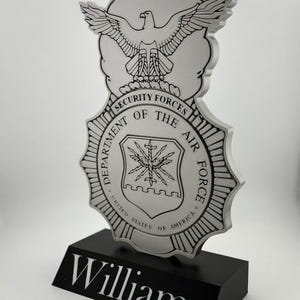 May include: A silver metal plaque with the Department of the Air Force Security Forces emblem. The plaque has a black base with the name "Williams" engraved on it.