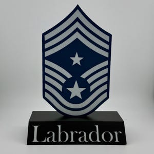 Pode incluir: Uma insígnia de posto militar azul e branca com duas estrelas em uma base preta com a palavra "Labrador" em letras brancas.