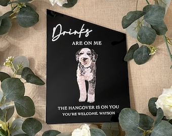 May include: Black sign with white text that reads "Drinks are on me. The hangover is on you. You're welcome, Watson." A black and white dog is pictured in the middle of the sign.