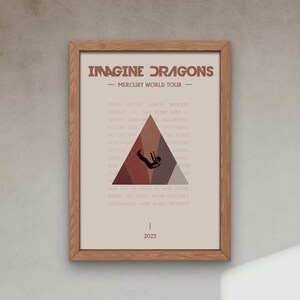 Pode incluir: Um cartaz bege com um tri&acirc;ngulo castanho no centro. O tri&acirc;ngulo tem a silhueta de uma pessoa a cair. O cartaz tem o texto "Imagine Dragons - Mercury World Tour -" no topo e uma lista de t&iacute;tulos de m&uacute;sicas em fonte castanha. A parte inferior do cartaz tem o ano "2022".