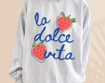 Peut inclure: Sweat-shirt gris avec le texte "la dolce vita" en écriture bleue et deux fraises rouges imprimées sur le devant.