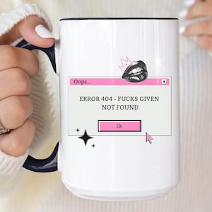 May include: White ceramic mug with a black rim and handle. The mug features a pink and black graphic with the text "Oops... ERROR 404 - FUCKS GIVEN NOT FOUND" and a pink "Ok" button.