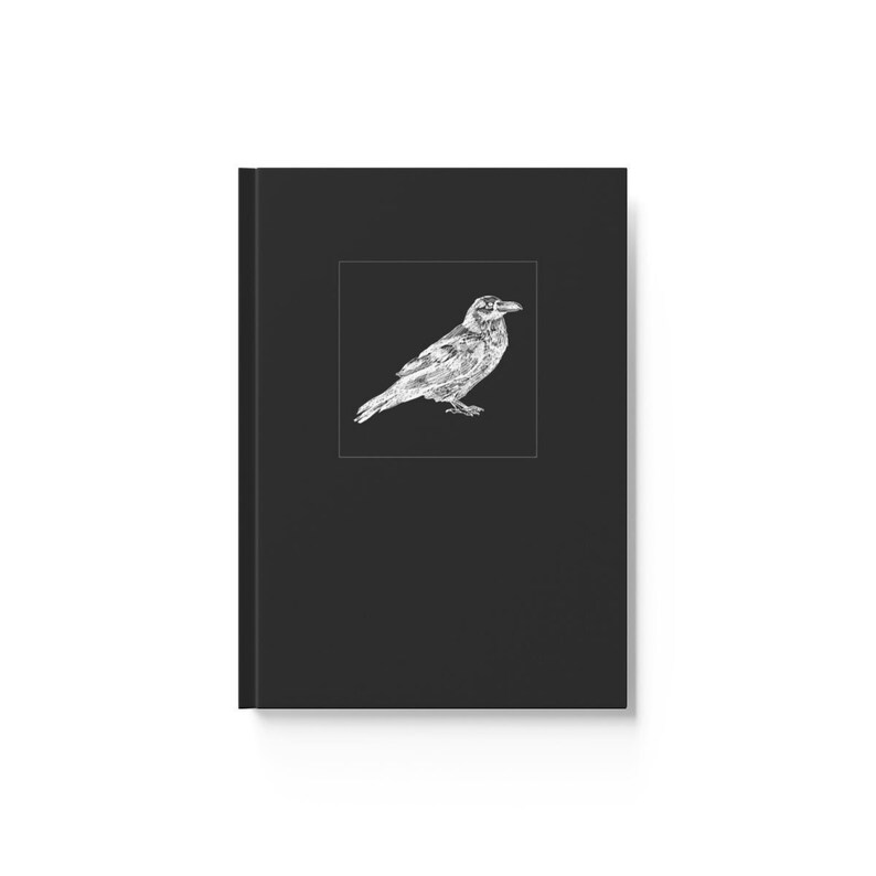 May include: Black journal with a white illustration of a raven on the cover. The raven is detailed with fine lines and is set against a black square. The journal is rectangular and has a clean, minimalist design.