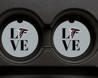 Puede incluir: Dos posavasos grises para coche con la palabra "LOVE" en letras negras y un logotipo de halcón rojo, negro y blanco. Los posavasos están en un portavasos negro para coche.