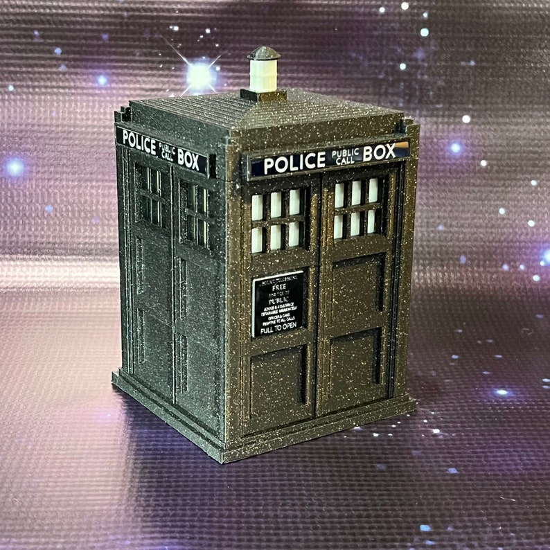 May include: A dark gray, textured, miniature replica of a police call box with the words "Police Public Call Box" printed on the front. The box has a small sign that reads "Free Parking For TARDIS Only.  All Other Vehicles Will Be Towed Away.  Pull To Open."