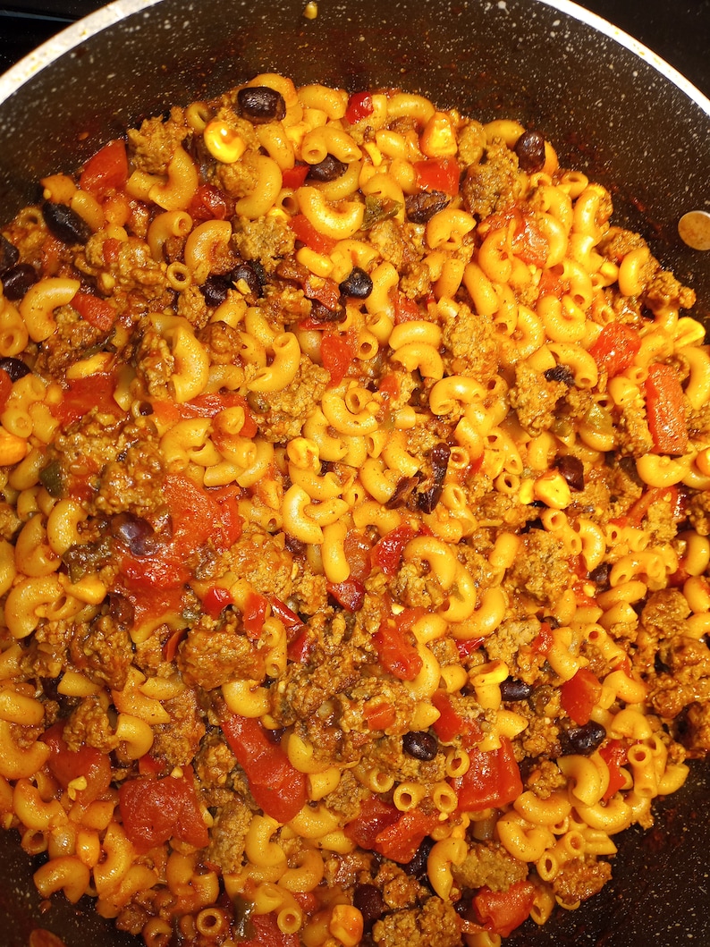 K&ouml;nnte beinhalten: Nahaufnahme eines Topfes gef&uuml;llt mit einer Mischung aus Makkaroni, Hackfleisch, schwarzen Bohnen, Mais und gew&uuml;rfelten Tomaten. Die Nudeln sind gekocht und die Zutaten sind in einer dicken Sauce vermischt.