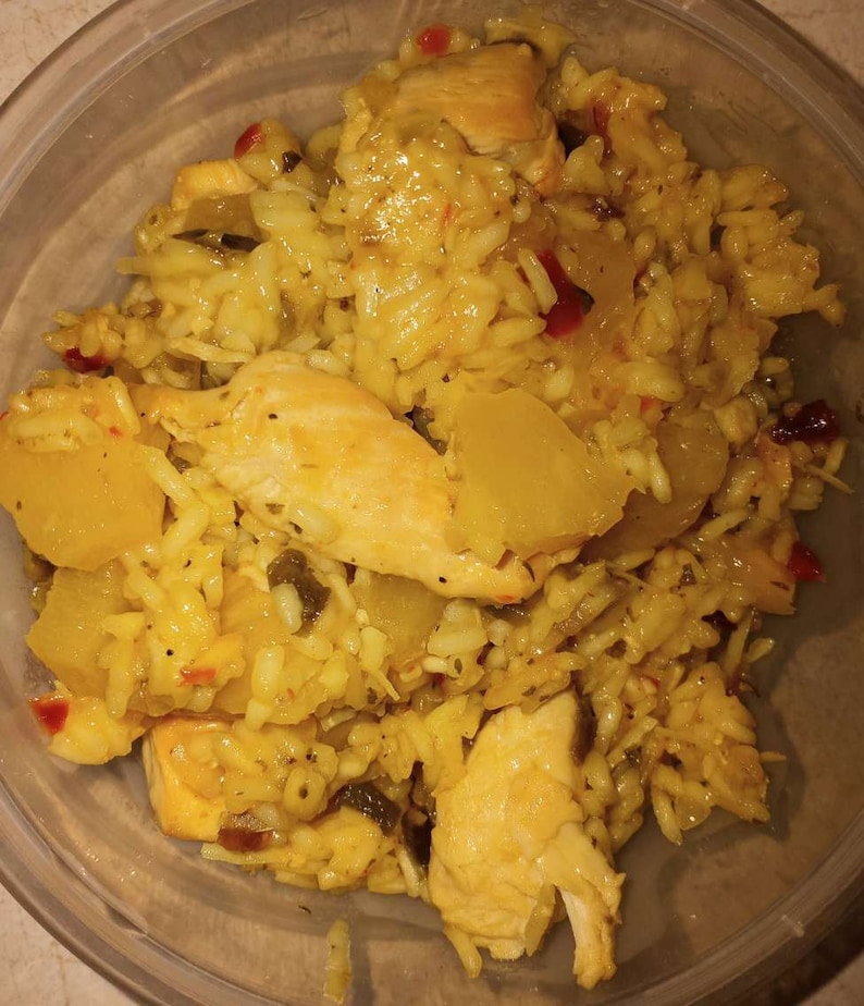 K&ouml;nnte beinhalten: Eine Nahaufnahme einer Sch&uuml;ssel mit gelbem Reis mit H&uuml;hnchen und Ananas. Der Reis ist gekocht und fluffig, und das H&uuml;hnchen ist zart und saftig. Die Ananas ist s&uuml;&szlig; und s&auml;uerlich, und das Gericht ist mit roten Pfefferflocken garniert.