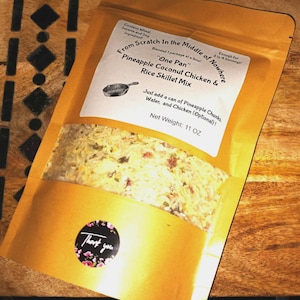 May include: A golden-colored pouch of "Pineapple Coconut Chicken & Rice Skillet Mix" with a clear window showing the contents. The label includes instructions and a net weight of 11 oz. A small sticker with the words "Thank you" is on the front.