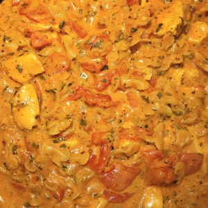 K&ouml;nnte beinhalten: Nahaufnahme eines cremigen Pastagerichts mit H&uuml;hnchen, Tomaten und Kr&auml;utern. Die Pasta ist al dente gekocht und die Sauce ist reichhaltig und geschmackvoll.