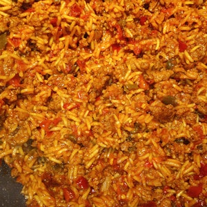 K&ouml;nnte beinhalten: Nahaufnahme einer Bratpfanne gef&uuml;llt mit einer Mischung aus gebratenem Hackfleisch, Reis und roten Paprikaschoten. Die Mischung ist mit einer roten Sauce gew&uuml;rzt und sieht nach einem herzhaften und schmackhaften Gericht aus.