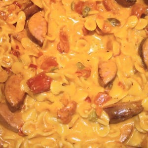 May include: Close-up of a pasta dish with sliced sausage, diced red tomatoes, and green peppers. The pasta is coated in a creamy, yellow sauce. The dish is a hearty meal.
