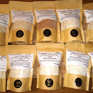 May include: Ten brown paper bags with white labels and black text. Each bag contains a different flavored instant oatmeal mix. The flavors include Cranberry Orange, Brown Sugar Cinnamon, Chocolate Coconut, Pumpkin, Cinnamon Raisin, Maple Pecan, Pineapple Coconut, Walnut Honey, White Chocolate & Almond, and Cranberry Walnut.