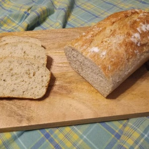 May include: A wooden cutting board with a loaf of white bread and slices of bread on it.