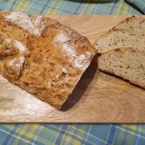 May include: A loaf of crusty bread with a golden brown crust, sliced on a wooden cutting board. The bread has a rustic appearance and is slightly dusted with flour.