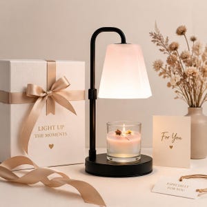 May include: A black metal candle warmer with a white lampshade, a lit candle in a glass, and a gift box with a ribbon. The gift box has the text "LIGHT UP THE MOMENTS". A card reads "For You".