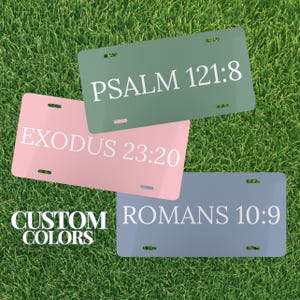 May include: Three license plates in shades of pink, green, and blue, each with white text. The plates display the text "PSALM 121:8", "EXODUS 23:20", and "ROMANS 10:9". The phrase "CUSTOM COLORS" is also visible.