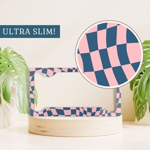 May include: A pink and blue checkered license plate frame with the text "ULTRA SLIM!" printed on the top. The frame is made of metal and has a glossy finish.
