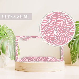 May include: A pink license plate frame with a white wave pattern. The frame is made of metal and has a slim design. The text "ULTRA SLIM!" is visible in the image.