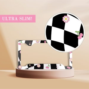 May include: A black and white checkered license plate frame with pink flowers and cherries. The frame is labeled "ULTRA SLIM!"