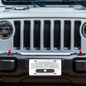 May include: A white Jeep Wrangler with a black grille and a number plate that reads "BOOKWORM" with a heart symbol.