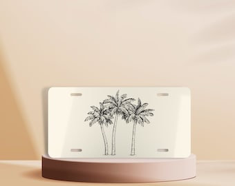 May include: White metal license plate with a black and white line drawing of three palm trees.