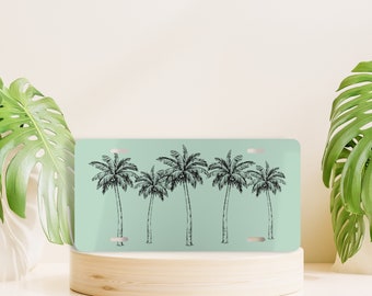 May include: A light blue license plate with a black and white illustration of five palm trees. The palm trees are drawn in a simple, stylized way.