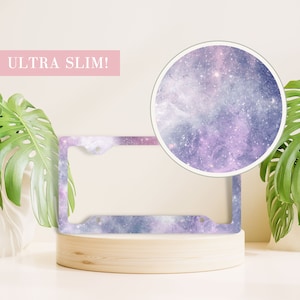 May include: A galaxy-themed license plate frame with a purple and blue color scheme. The frame is made of metal and has a slim design. The text "ULTRA SLIM!" is visible in the image.