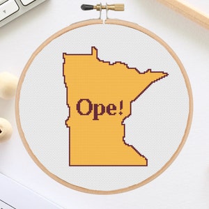Può includere: Un cerchio da ricamo bianco con un contorno giallo dello stato del Minnesota e la parola "Ope!" in testo nero.