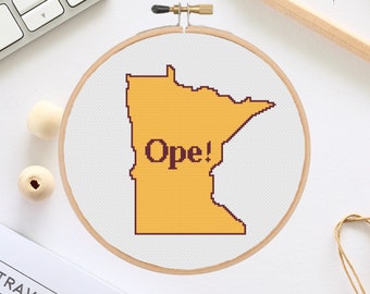 May include: A white embroidery hoop with a yellow outline of the state of Minnesota and the word "Ope!" in black text.