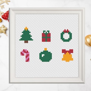 May include: A white frame with a white mat surrounding a cross-stitch design of six Christmas icons. The icons are a green Christmas tree, a red gift box, a green wreath with a red bow, a pink candy cane, a green Christmas ornament, and a yellow bell with a red bow.