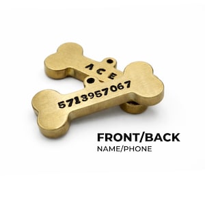 Two gold-colored, bone-shaped pet tags. One tag is stacked on top of the other. The top tag has the name "ACE" engraved on it. The bottom tag has the phone number "5713957067" engraved on it. The text "FRONT/BACK NAME/PHONE" is below the tags. Custom dog ID tag engraved with pet name and phone number, personalized dog tags for pets