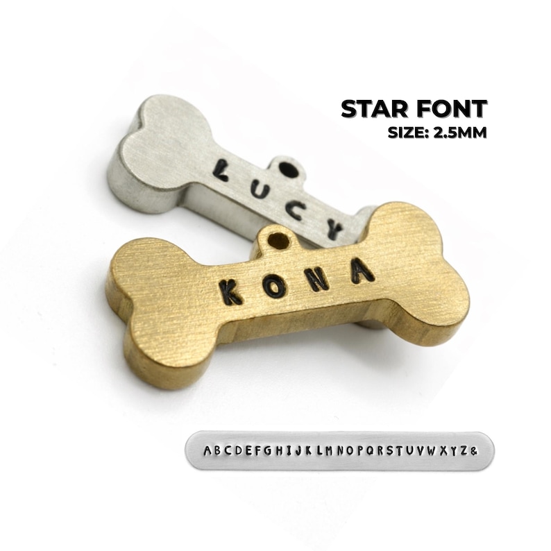 Two bone-shaped pet tags, one silver and one gold, with the names "LUCY" and "KONA" stamped on them. The text "STAR FONT SIZE: 2.5MM" is above the tags. A metal strip with the alphabet is below the tags. Custom brass dog tags personalized for pets showing star font engraving style