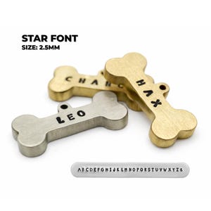 Bone-shaped pet tags in brass and silver tones, engraved with names. The tags are in a star font and are 2.5mm in size. A small metal strip with the alphabet is also included. Star font example for engraved dog name tags personalized for pets on brass and silver dog tags