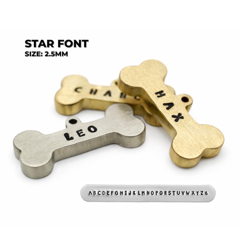 Bone-shaped pet tags in brass and silver tones, engraved with names. The tags are in a star font and are 2.5mm in size. A small metal strip with the alphabet is also included. Star font example for engraved dog name tags personalized for pets on brass and silver dog tags