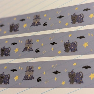 May include: Three strips of washi tape with a purple background and a repeating pattern of a black cat wearing a purple wizard hat and a yellow star. The cat is holding a wand. There are also bats and yellow stars on the tape.
