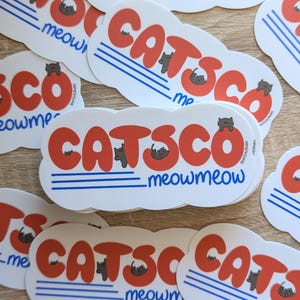 May include: A stack of white oval stickers with a red, white, and blue design. The stickers feature the text "CATSCO meowmeow" with a cartoon cat illustration.