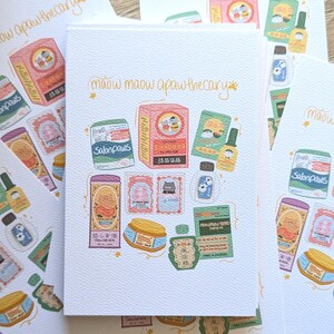 May include: A stack of white cards featuring colorful illustrations of cat-themed apothecary products. The cards display text in English and other languages, including "maow maow apaw thecary" and "Salonpaws."