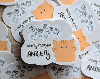 May include: A stack of stickers featuring a cartoon orange cat with a thought bubble filled with various icons. The text on the sticker reads "many thoughts, ANXIETY".