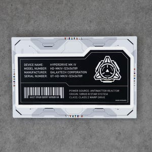 May include: A rectangular label with a white and gray mechanical border featuring the text HYPERDRIVE MK IV, model number HD-MKIV-123456789, manufacturer GALAXTECH CORPORATION, serial number GT-HD-MKIV-123456789, a barcode, and an antimatter reactor icon.