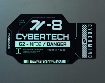 Può includere: Un adesivo rettangolare nero con angoli arrotondati che presenta testo e grafiche bianche. Mostra il testo 77-8, CYBERTECH, G2-NF32 / DANGER, VANGUARD e CYBERMIND. Include marcature tecniche, un simbolo di pericolo e un codice a barre in basso.