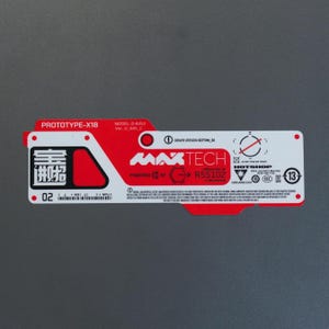 Könnte beinhalten: Ein rechteckiger, rot-weißer Aufkleber mit der Aufschrift PROTOTYPE-X18, MAXTECH und R55102. Das Etikett enthält verschiedene technische Symbole, einen Strichcode, die Zahl 02 und kleine Warnhinweise in Englisch sowie ein schwarzes Logo links.