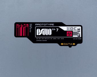 May include: A rectangular black sticker with rounded edges featuring white text that reads PROTOTYPE, SN-7, and DO NOT USE OUTLETS OR CORDS THAT HAVE EXPOSED WIRING. It includes a red barcode, a red square icon, and the yellow text DATA.