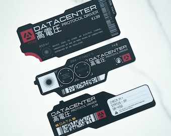May include: Three black rectangular stickers with notched edges, featuring white text including DATACENTER PROTOCOL DRIVER, Japanese characters, barcodes, and technical diagrams. The designs include red accents, serial numbers, and check-in fields.